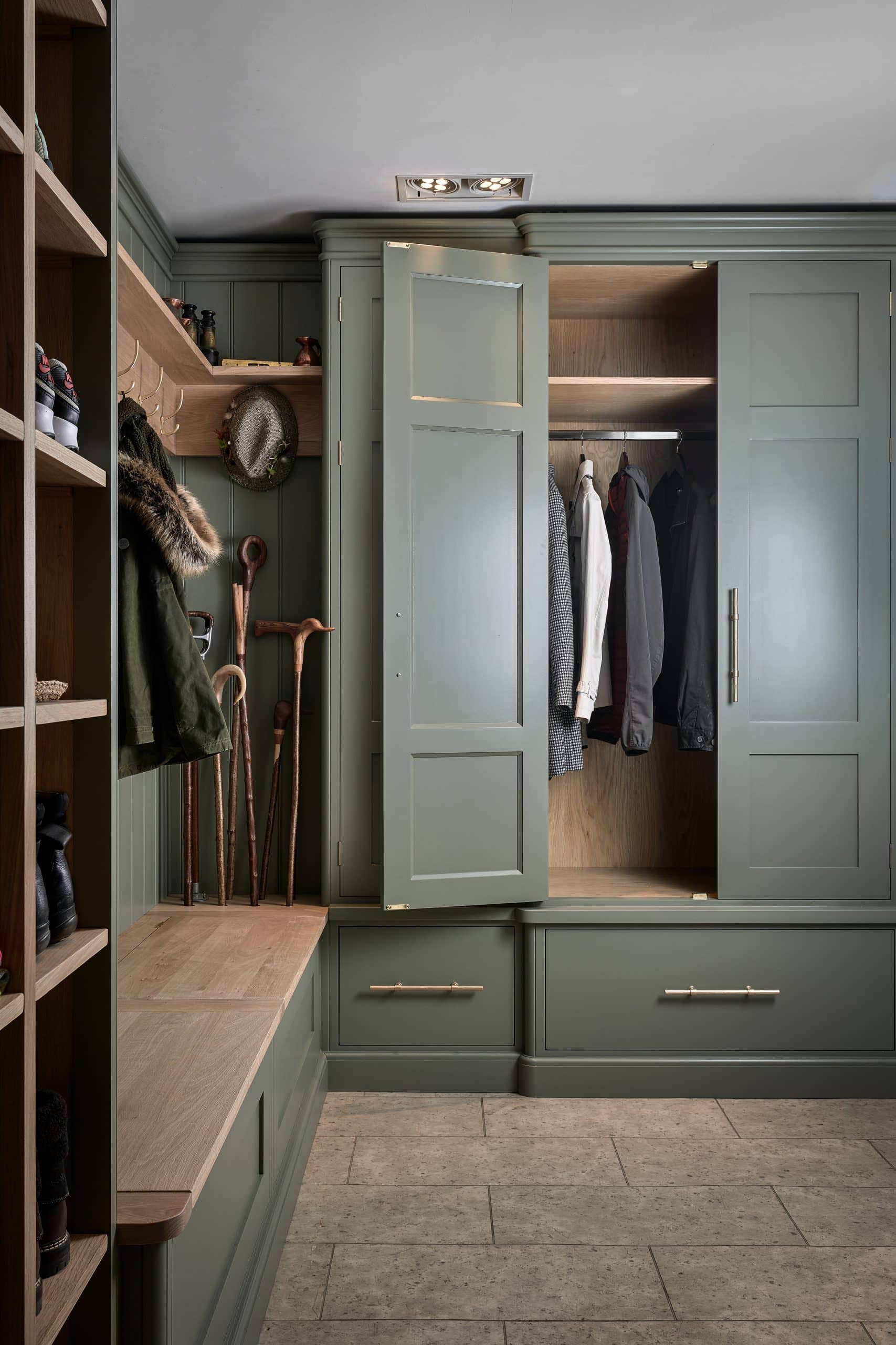 Boot room with hanging coats in cupboard and oak bench seating.